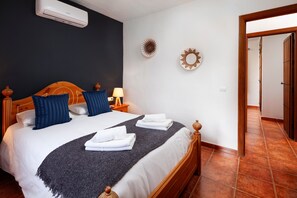 Habitación de hotel con una cama, una mesita de noche, una lámpara y aire acondicionado instalado en la pared.
