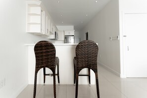A modern kitchen with white cabinetry and a central island. There are two wicker chairs with curved backs.
