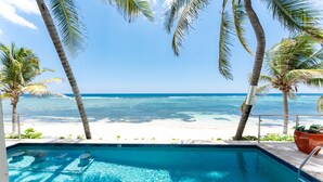 A pool with a view of the ocean and beach, surrounded by palm trees.