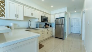 A modern kitchen with white cabinetry, stainless steel appliances, and a clean, tiled floor.