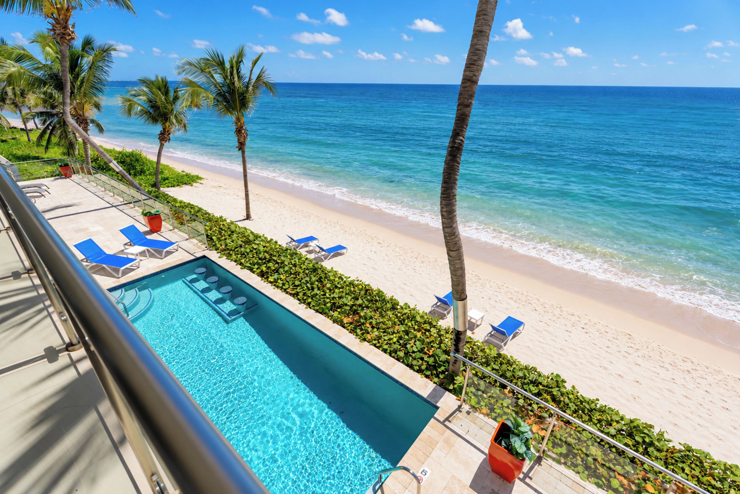 A poolside view with a clear blue ocean and a sandy beach.
