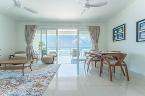A spacious living area with a balcony overlooking the sea, furnished with a dining table, chairs, and sofas.