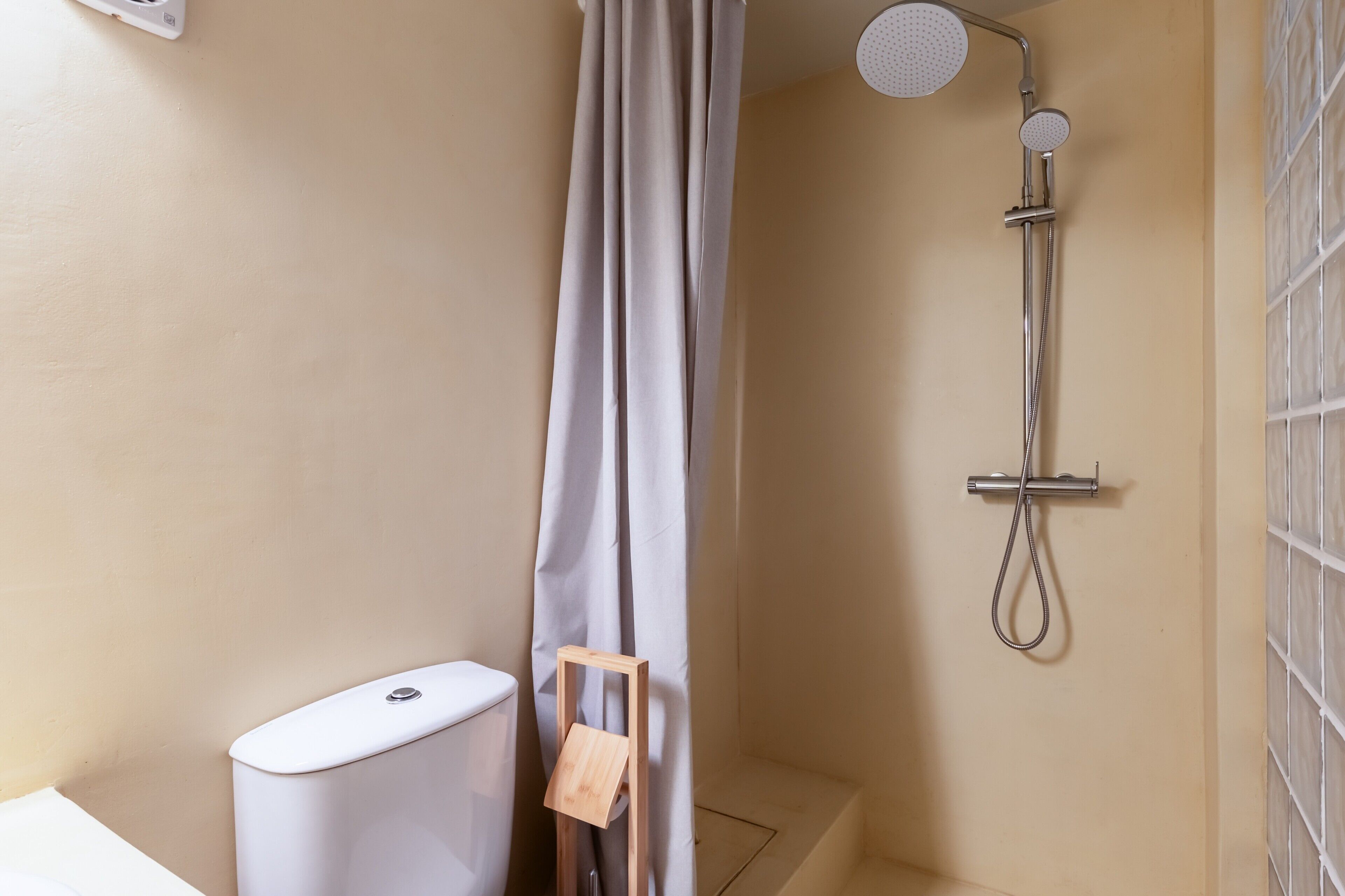 Un baño con ducha, inodoro y un taburete de madera.