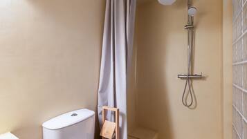 Un baño con ducha, inodoro y un taburete de madera.