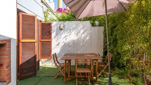 Eine Terrasse mit Tisch und Stühlen, eine Holztür und eine weiße Wand.