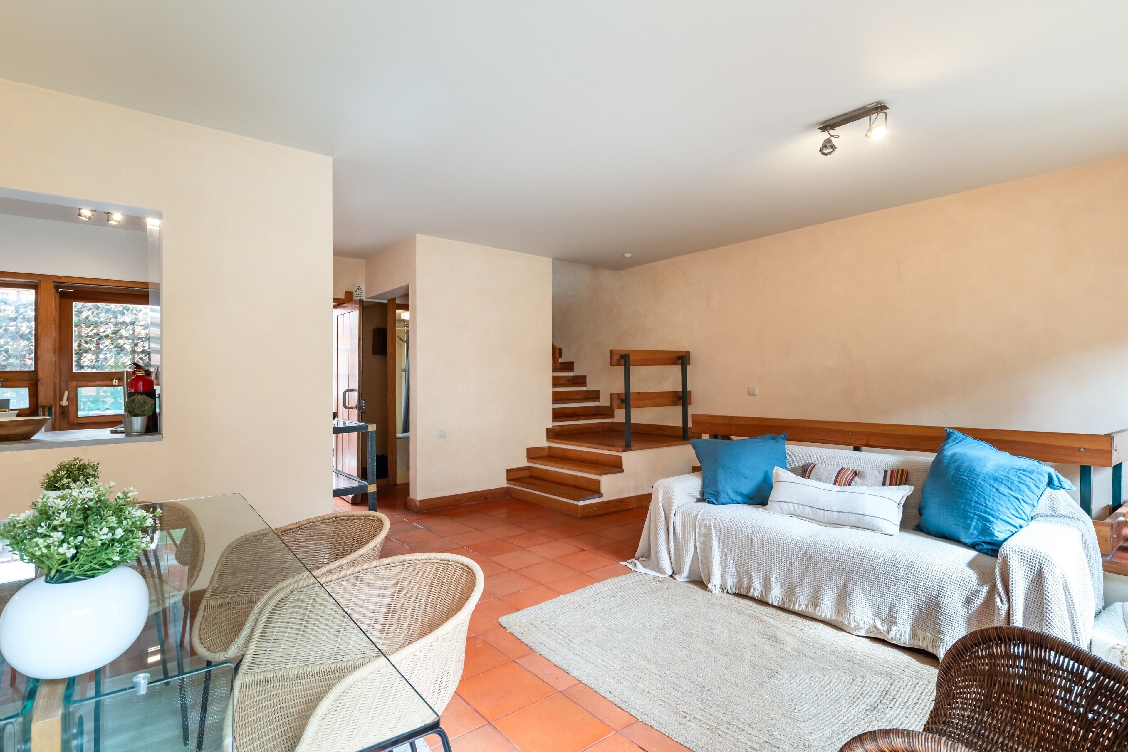 Een ruime woonkamer met een zithoek, een eettafel met stoelen en een trap naar een hoger gelegen verdieping.