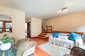 Een ruime woonkamer met een zithoek, een eettafel met stoelen en een trap naar een hoger gelegen verdieping.