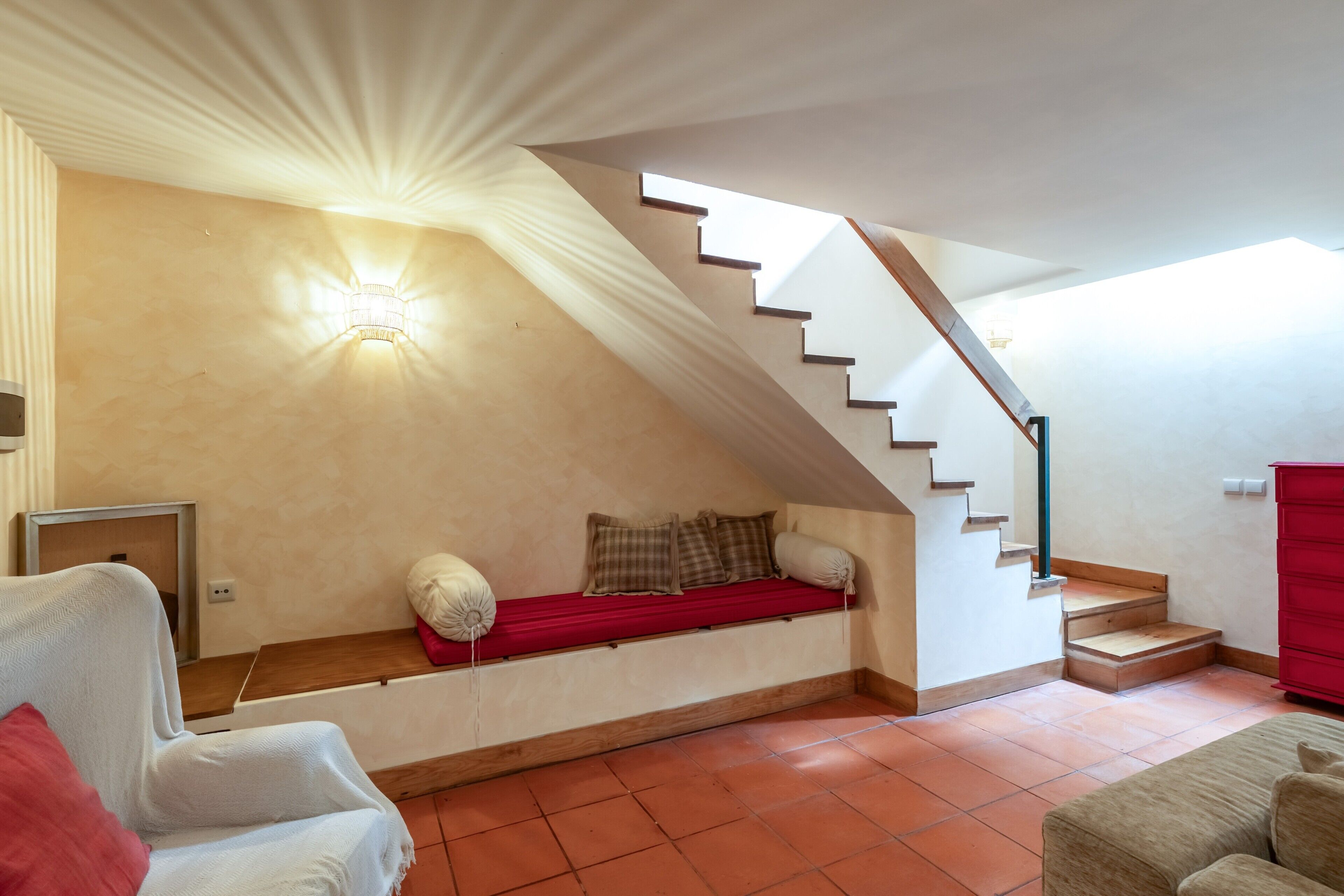 Une pièce avec un plafond en pente, un escalier, un lit avec des oreillers et un banc rouge.