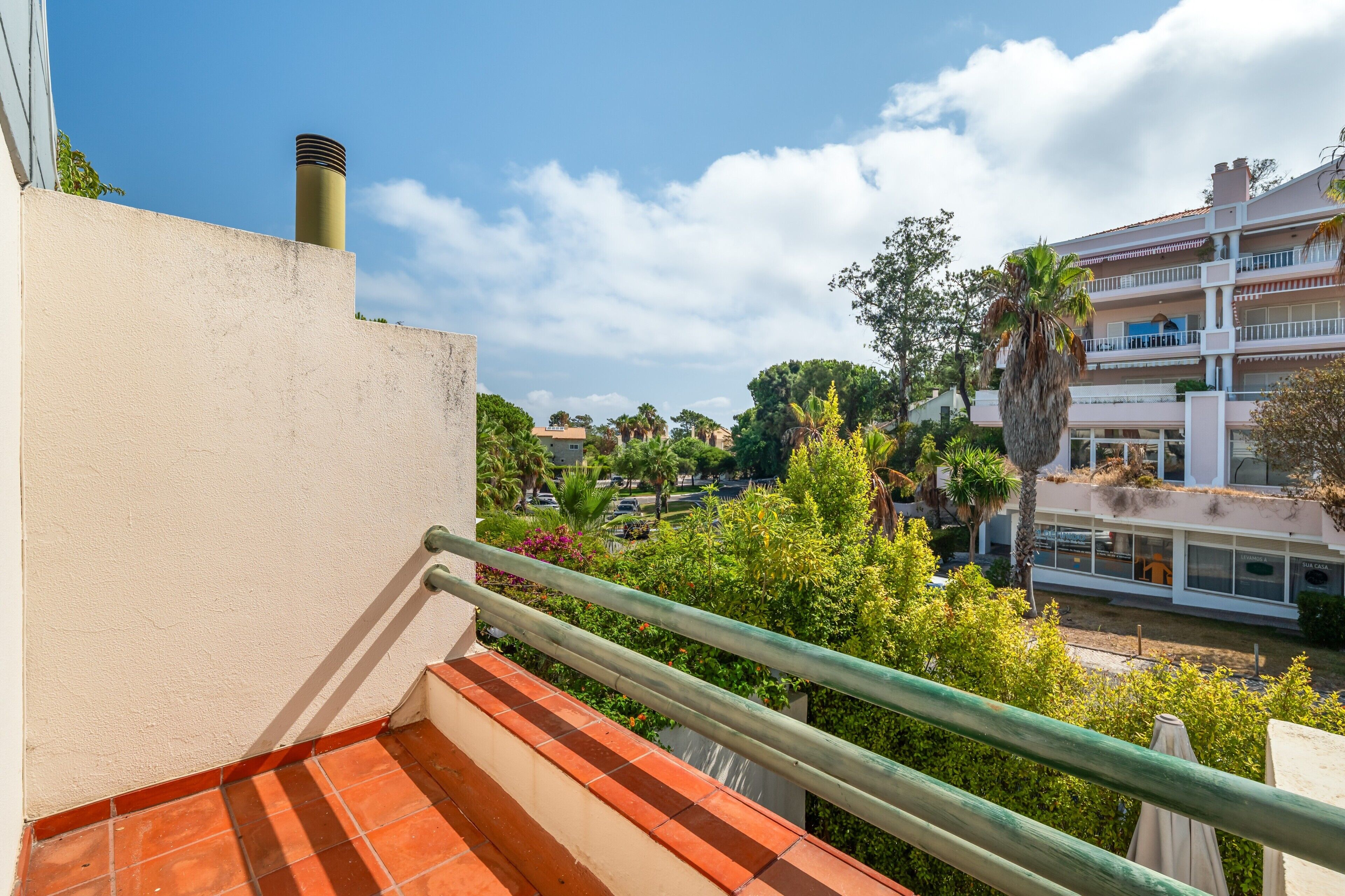 A balcony with a tiled floor, a metal railing, and a view of a residential area with houses and trees.