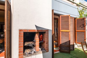 Een buitenbarbecue van baksteen, met een houten luik, een kleine bakstenen oven en een houten stoel.