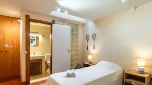 A hotel room with a bed, a bedside table with a lamp, a bathroom with a sink and toilet, and a wooden wardrobe.