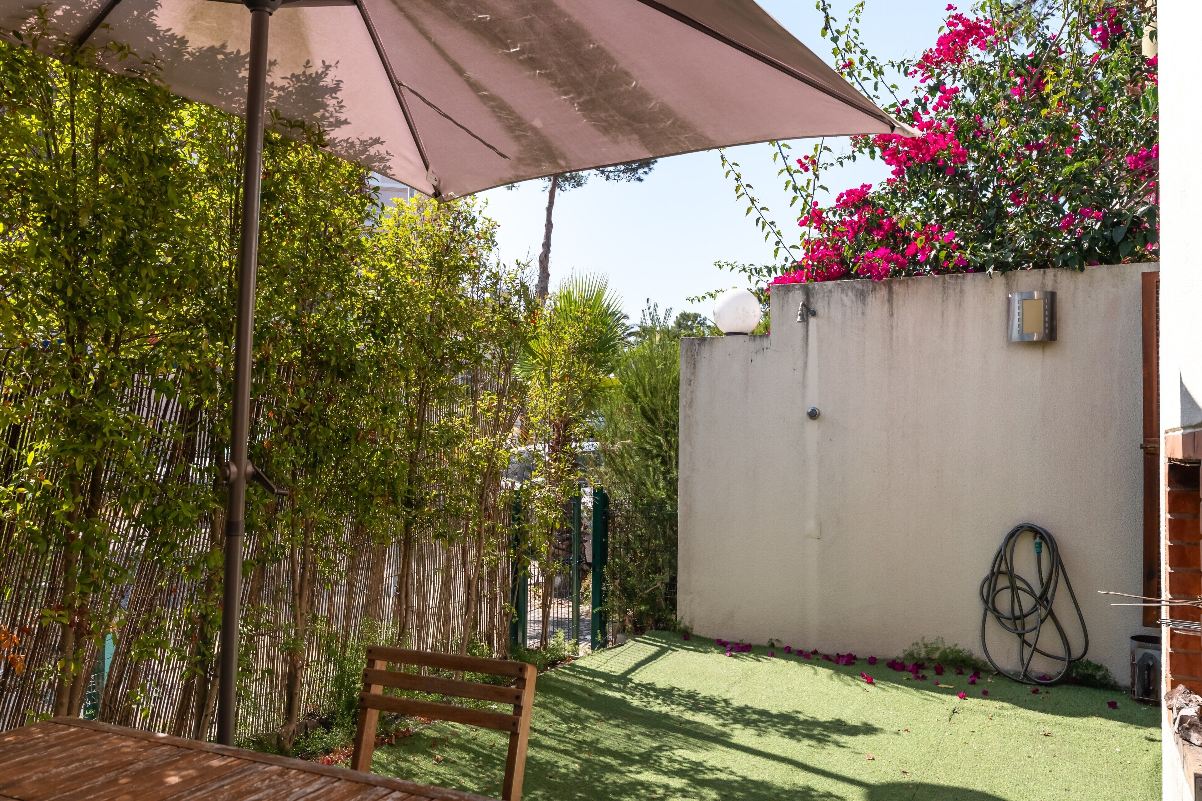 Een terras met een houten bank, een tafel en een grote parasol.