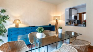 A modern dining area with a glass table, wicker chairs, a blue cabinet, and a lamp.
