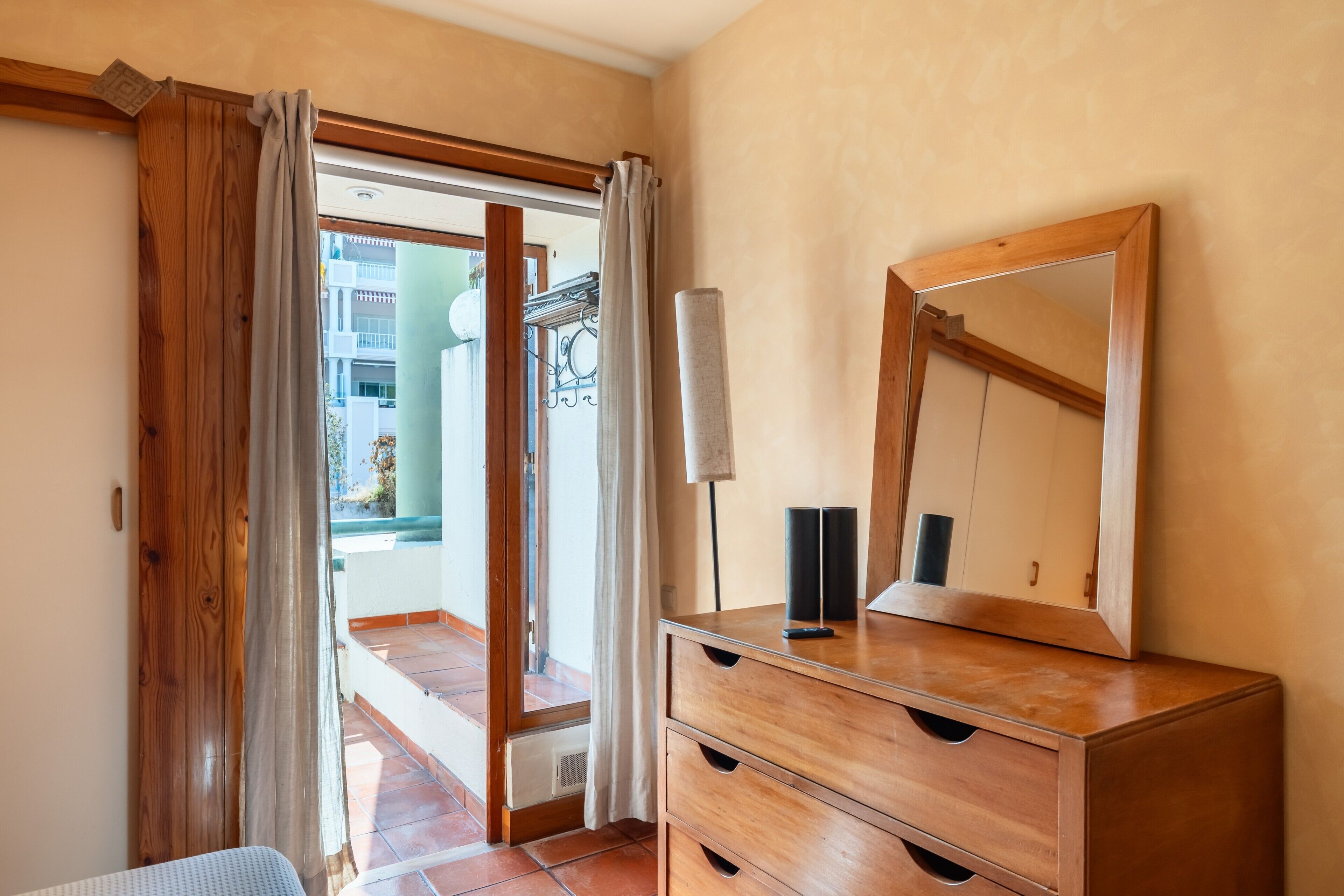 Una habitación con un aparador de madera, un espejo y una puerta corrediza de vidrio que da a un espacio exterior.