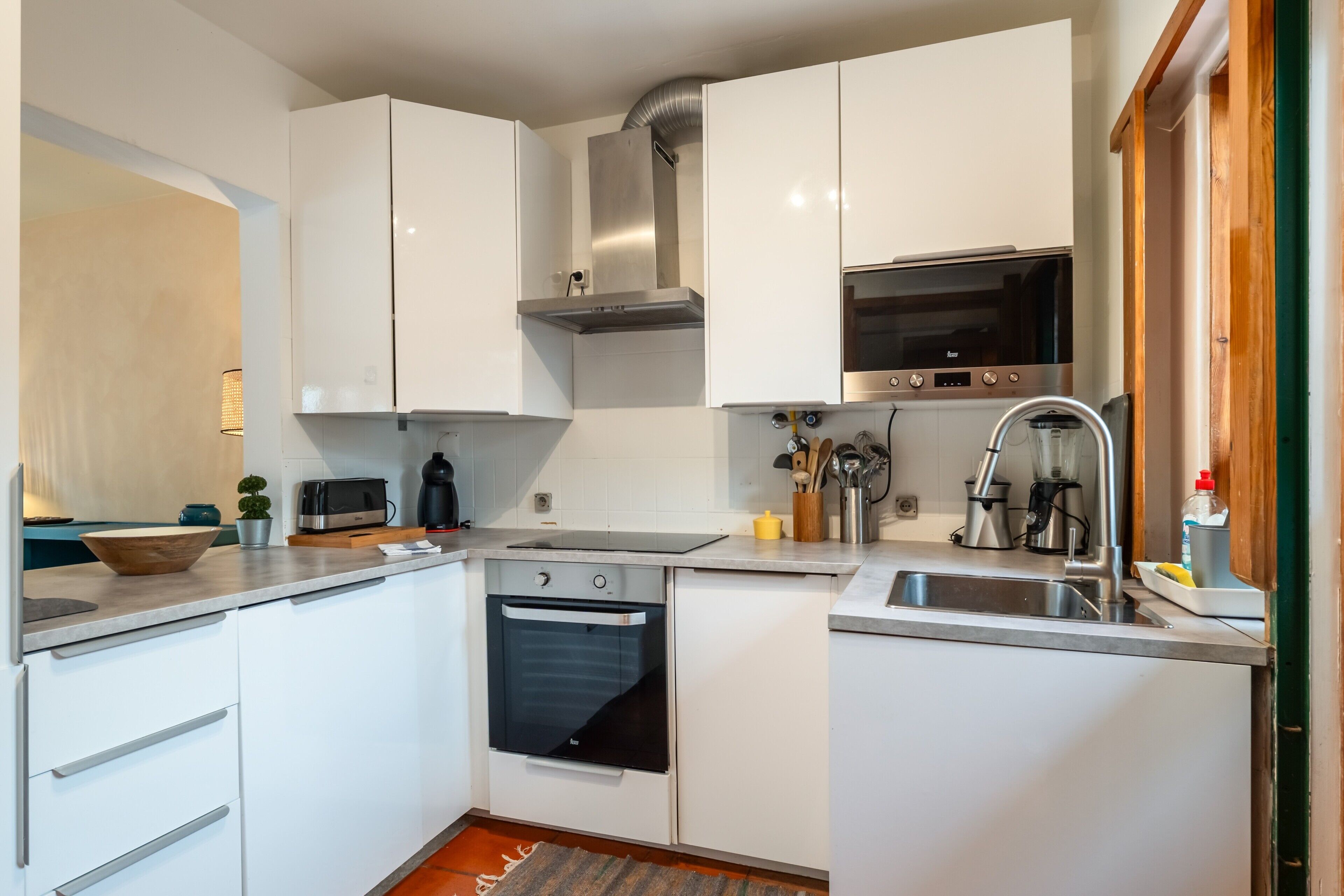 Een kleine keuken met witte kastjes, een inbouwoven, een magnetron en een roestvrijstalen afzuigkap.