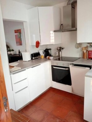 Una cocina compacta con armarios blancos, horno empotrado, cafetera y tostadora.