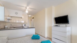 A modern hotel room with a kitchenette, a flat-screen TV, a bed with patterned bedding, and a ceiling fan. - Vacation 'Castle Harbour' with Sea View, Shared Pool and Private Terrace (Los Cristianos)