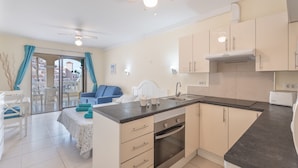 A modern kitchen with a central island, a dining area with a table and chairs, and a view through a glass door to the outside. - Vacation 'Castle Harbour' with Sea View, Shared Pool and Private Terrace (Los Cristianos)