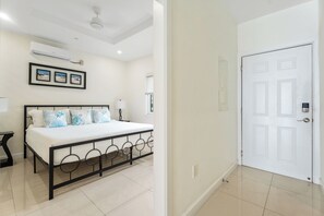 A bedroom with a bed, a ceiling fan, an air conditioning unit, and a door.