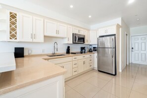 A modern kitchen with white cabinetry, stainless steel appliances, and a tiled floor.