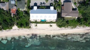 An aerial view of a beachfront property with a large house, a swimming pool, and a sandy beach.