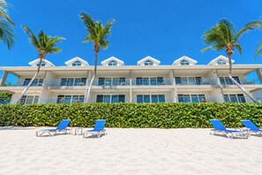 Un hôtel en bord de mer doté de nombreux balcons, de palmiers et de chaises longues.