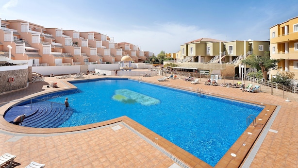 A swimming pool with a tiled deck, lounge chairs, and a building with balconies in the background. - Vacation Apartment 'Orlando 103' with Shared Pool, Private Terrace and Wi-Fi (Adeje)