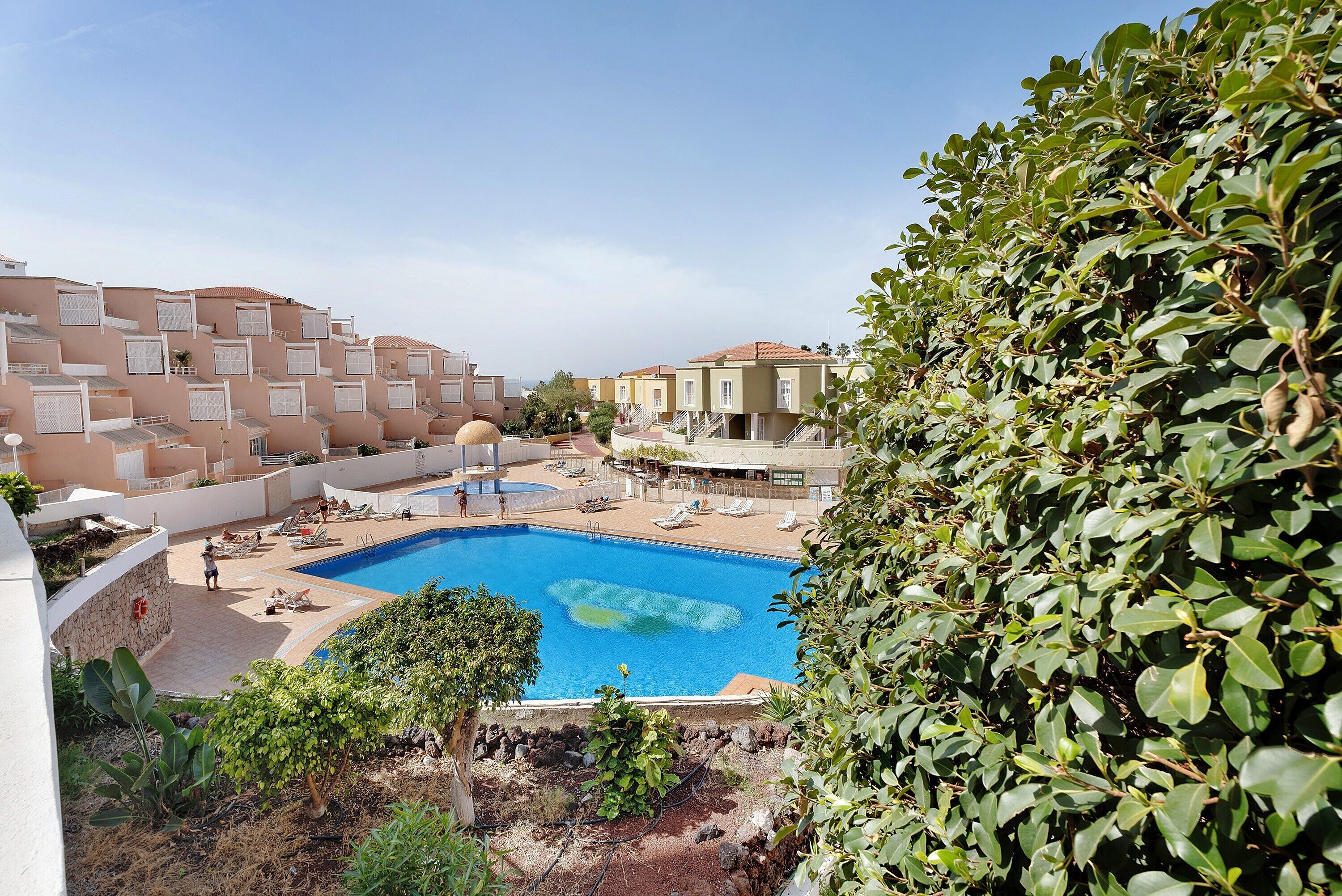 Una piscina rodeada de edificios, cielo despejado y vegetación.