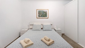 A bedroom with a bed, two pillows, a bedside table with a lamp, a framed picture on the wall, and a towel on the bed. - Vacation Apartment 'Orlando 103' with Shared Pool, Private Terrace and Wi-Fi (Adeje)