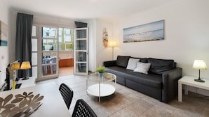 A modern living room with a sofa, a round glass coffee table, a dining table with chairs, a lamp, and a painting on the wall. - Vacation Apartment 'Orlando 103' with Shared Pool, Private Terrace and Wi-Fi (Adeje)