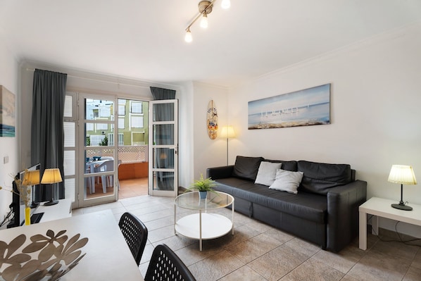 Un salon moderne avec un canapé, une table basse ronde en verre, une table à manger avec des chaises, une lampe et un tableau au mur.