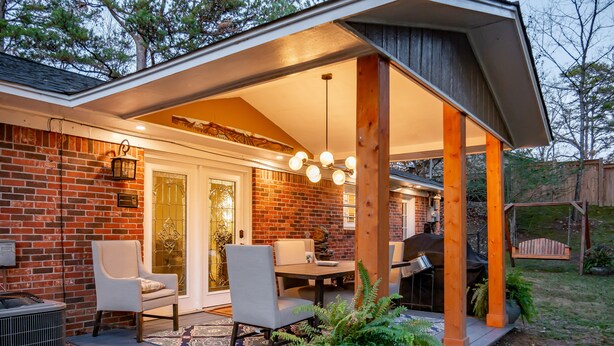 Un patio couvert avec un mur en briques, une table à manger avec des chaises et un barbecue.