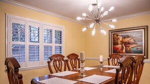 Une salle à manger avec une table en bois dressée pour quatre personnes, entourée de chaises décorées.