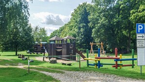 Ein Spielplatz mit einer Holzspielgeräte-Anlage, Schaukeln und einer Rutsche.