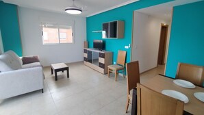 A living room with a sofa, a small table, a TV, and a dining area with chairs and a table.
