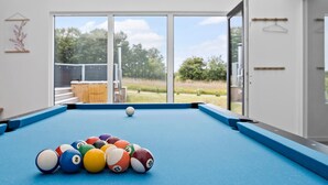 Ein Billardtisch mit Kugeln in einem Raum mit großen Fenstern und Blick ins Freie.