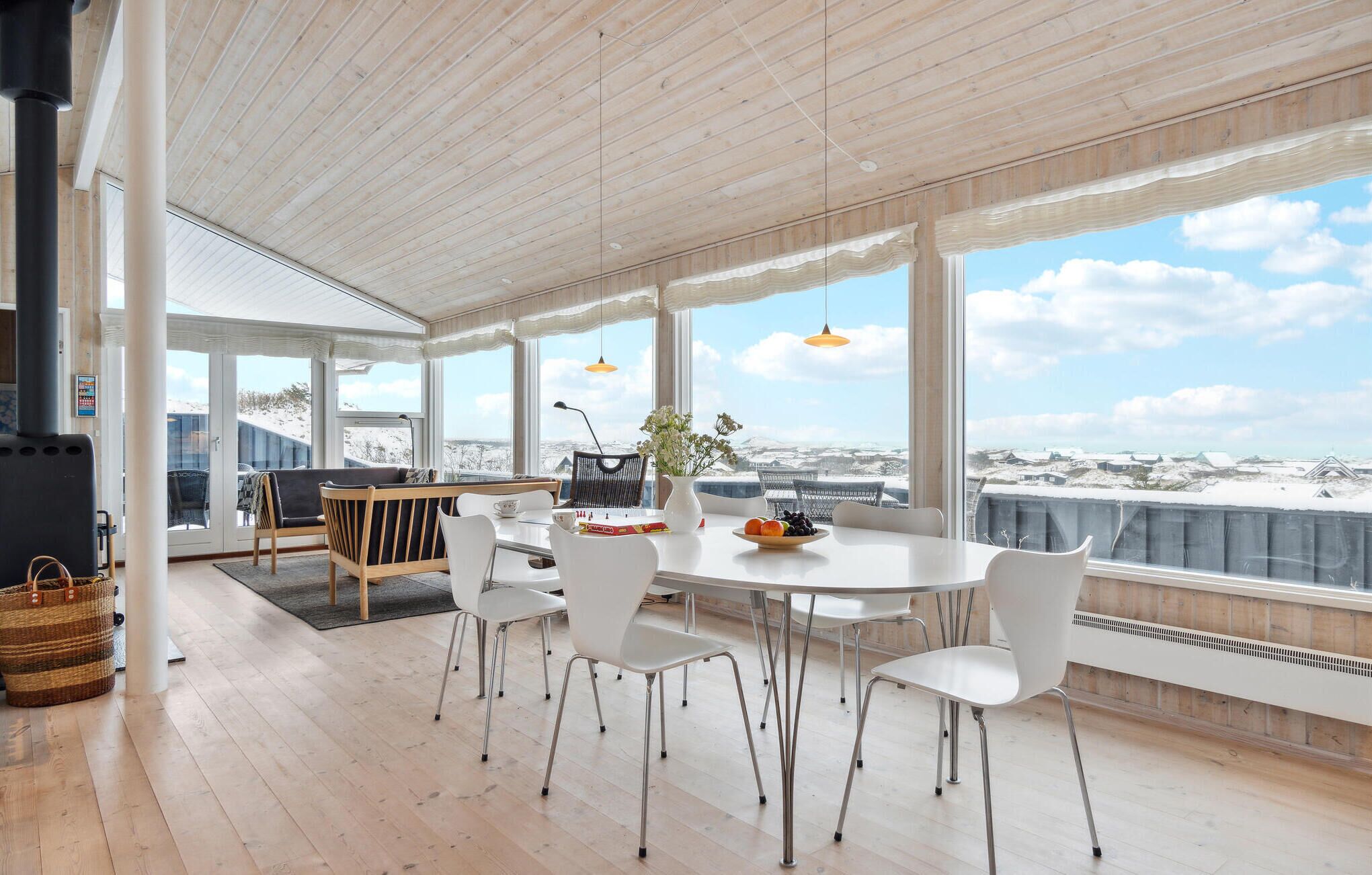 A spacious dining area with a view of the snowy landscape, wooden flooring, and modern white furniture.