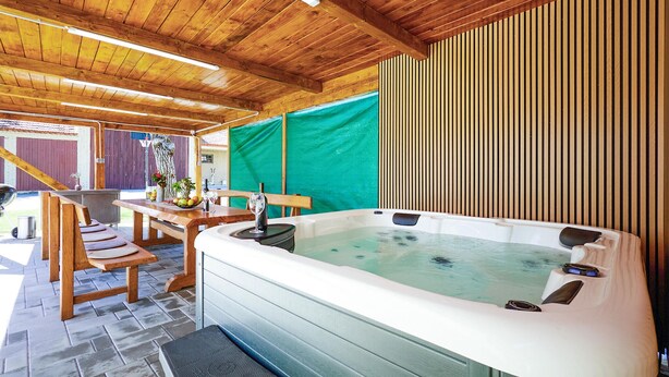 A wooden deck with a hot tub, a table with chairs, and a covered area with a green tarp. - Awesome home in Ivanska (Ivanska)