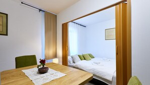 A hotel room with a wooden table, a vase with flowers, a bed with white bedding and green pillows, and a window with curtains. - Awesome home in Ivanska (Ivanska)