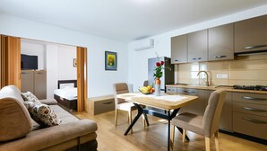 A modern hotel room with a wooden dining table, two chairs, a sofa, a TV, and a kitchen area with cabinets and a sink. - Awesome home in Ivanska (Ivanska)