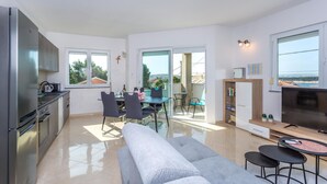 Un apartamento moderno con cocina, comedor y sala de estar. Cuenta con un amplio ventanal con vistas al mar, un sofá y un televisor.