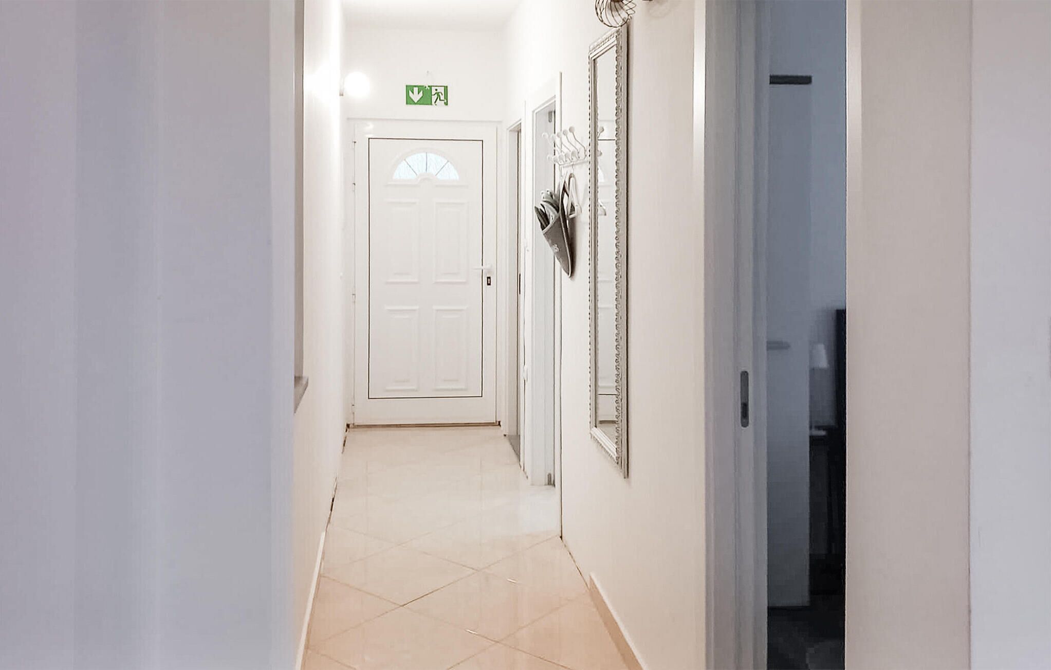 A hallway with a white door at the end, a coat rack, and a mirror on the wall.