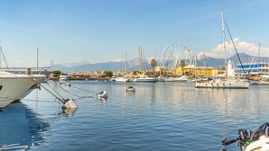 A marina with boats docked, a Ferris wheel, and mountains in the background. - Cozy apartment in Capezzano Pianore (Capezzano Pianore)