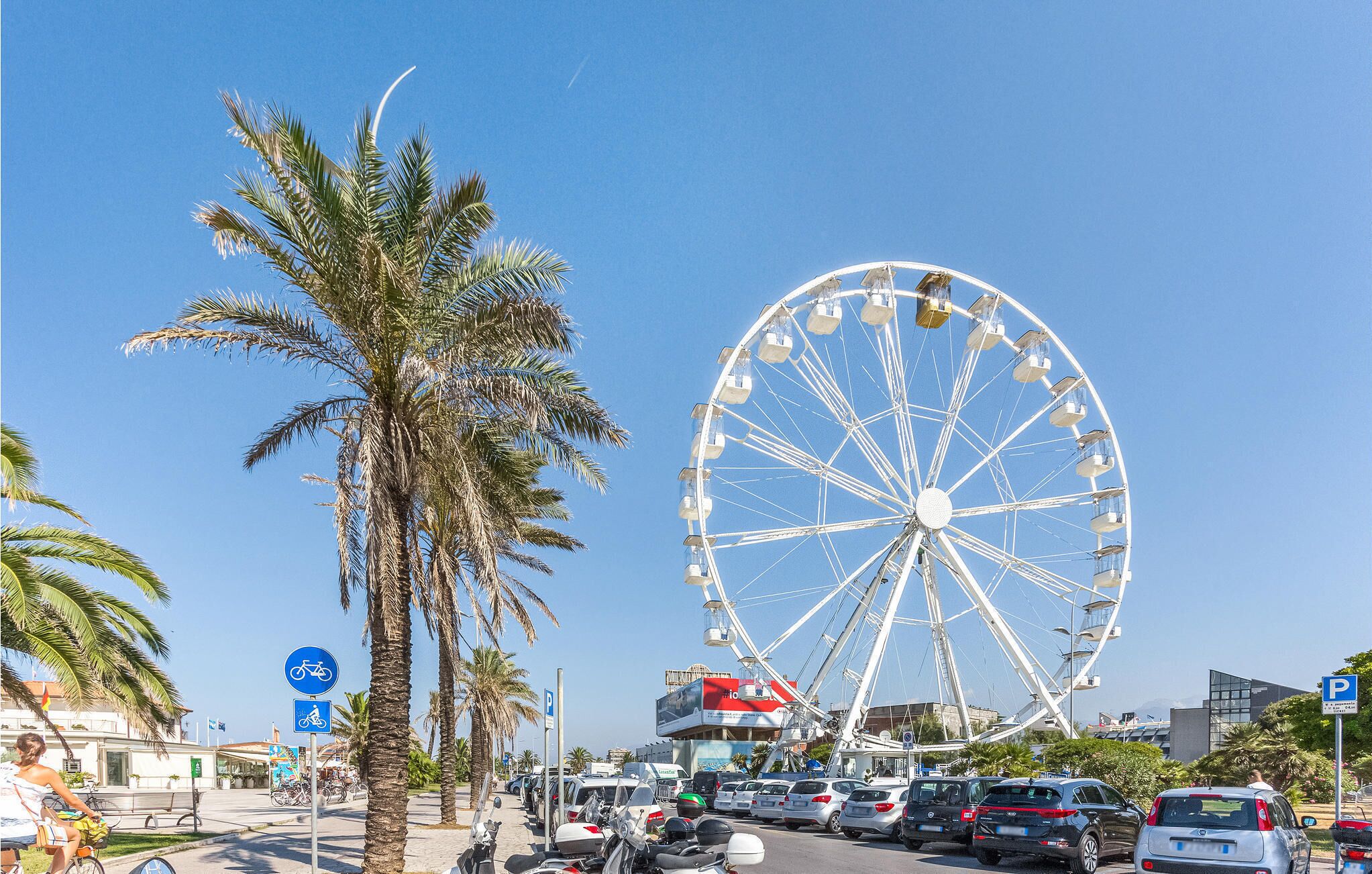 A busy street with a large Ferris wheel, palm trees, and a parking sign.