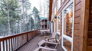 A wooden deck with Adirondack chairs, a wooden railing, and a view of a forested area. - Snow Banks Lodge, Beautiful Home in Angel Fire (Angel Fire)