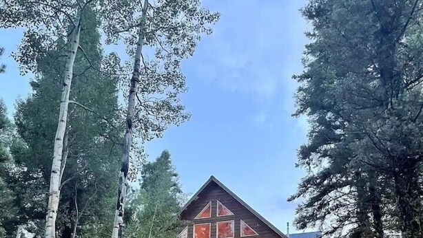 A wooden cabin with a balcony, surrounded by trees and string lights. - Snow Banks Lodge, Beautiful Home in Angel Fire (Angel Fire)