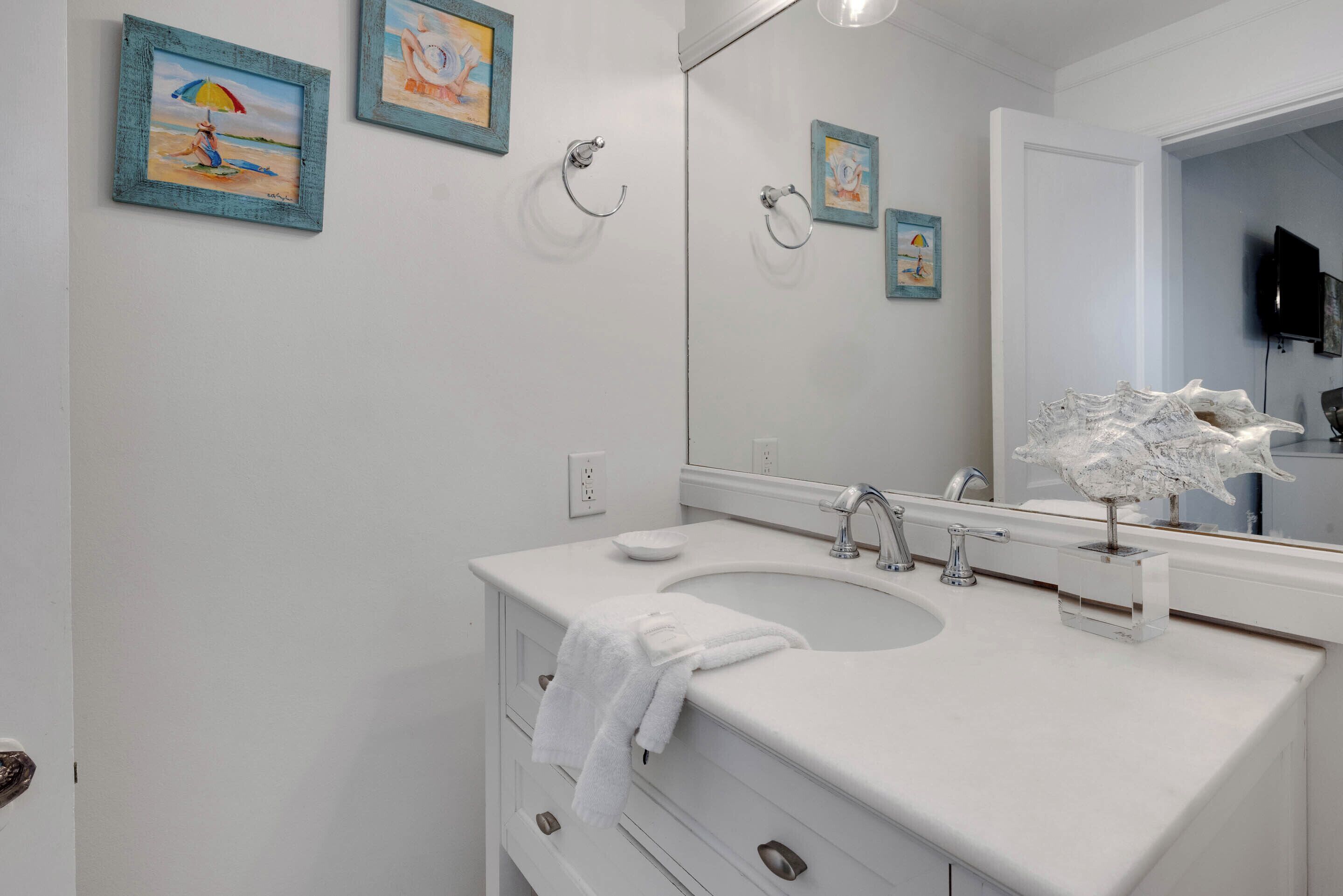 A bathroom with a white sink, a large mirror, and three framed beach paintings on the wall.