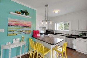 A kitchen with a teal accent wall, a painting, a seahorse decoration, and a bright yellow chair. - After Dune Delight by Tybee Vacation Rentals (Tybee Island)