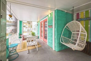 A covered outdoor seating area with white chairs and a hanging chair, a teal wall, and a sign that reads "BEACH HOUSE". - After Dune Delight by Tybee Vacation Rentals (Tybee Island)