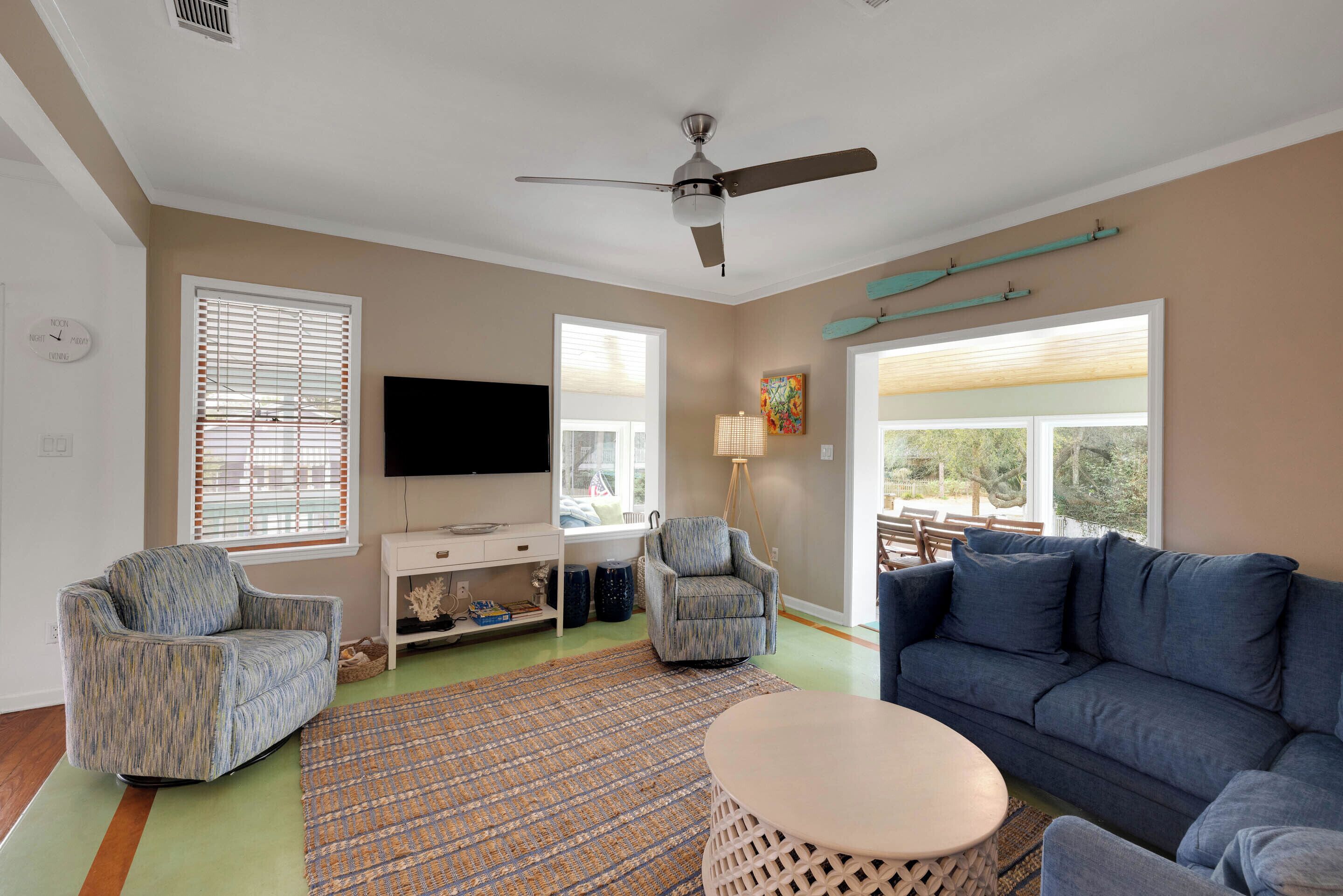 A living room with a ceiling fan, two armchairs, a sofa, a TV, a desk, and a window with blinds.